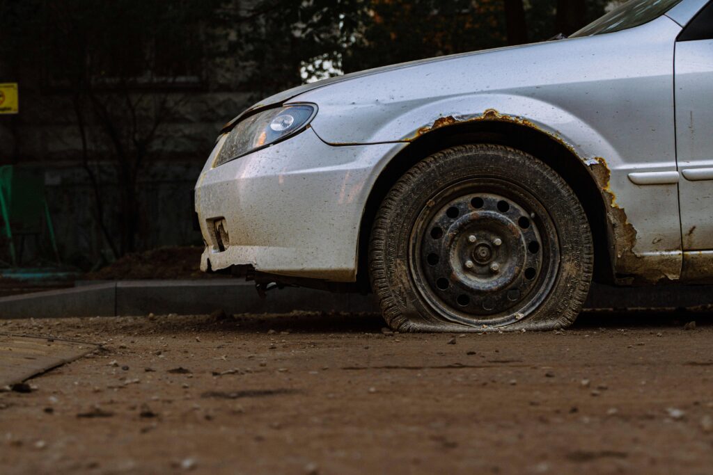 Close-up of a rusted car with a flat tire parked on a street in Moscow, illustrating urban decay.